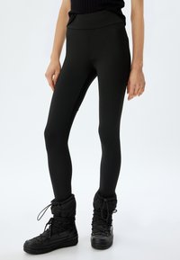Zwarte leggings van rekbare stof, met een hoge taille, gladde textuur, gecombineerd met zwarte, gevoerde enkellaarsjes met veters.