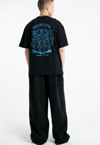 Czarna bawełniana koszulka z dużą niebieską grafiką tygrysa oraz napisem "RELENTLESS" na plecach. Połączona z luźnymi czarnymi spodniami.