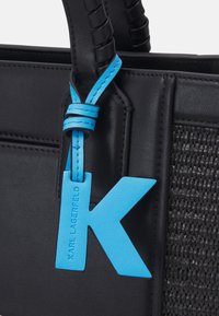 Sac en cuir noir avec panneau texturé et étiquette en cuir bleu vif en forme de "K" embossée du nom « Karl Lagerfeld », suspendue à la poignée.