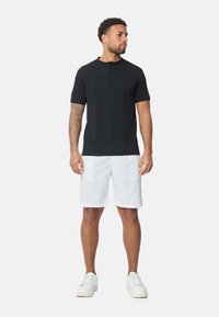 T-shirt henley noir à manches courtes avec trois boutons, associé à un short blanc jusqu'aux genoux et des baskets blanches ; texture lisse, coupe décontractée.