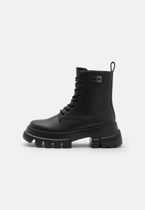 Bottines noires en cuir avec une semelle épaisse, dotées d'un design à lacets, d'une boucle à l'arrière et d'un logo de marque discret sur le côté.