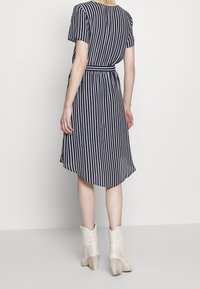 Navy and white striped dress with short sleeves, belted waist, and flowing A-line skirt. Paired with cream heeled boots.