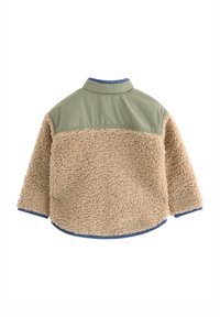 Faux fur jas heeft een beige, pluizige textuur op het lichaam, met een groene nylon bovenkant en blauwe afwerking op de manchetten en zoom.