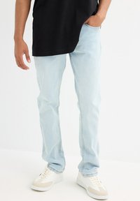 Unos vaqueros de denim azul claro con un dise�ño de pernera recta, que cuentan con bolsillos estándar y un dobladillo deshilachado, combinados con zapatillas blancas.
