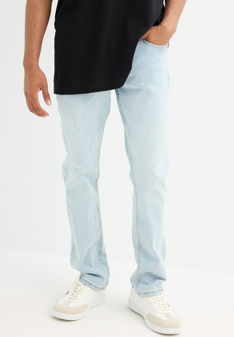 Unos vaqueros de denim azul claro con un diseño de pernera recta, que cuentan con bolsillos estándar y un dobladillo deshilachado, combinados con zapatillas blancas.
