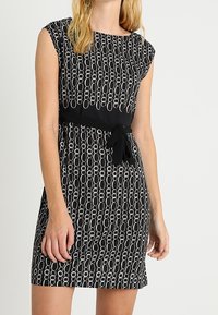 Czarna sukienka z białym okrągłym wzorem łańcucha, z krótkimi rękawami i dopasowanym krojem w talii, podkreślona wiązanym paskiem.