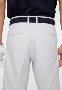 Ljusgrå byxor med en strukturerad yta, parat med ett flätat marinblått bälte. Har dubbla bakfickor och en kroppsnära passform.