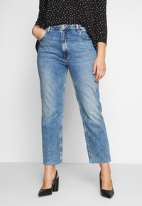Jeans de denim azul claro con pierna recta y dobladillo sin rematar. Combinados con una blusa negra de lunares y zapatos de tacón alto negros.
