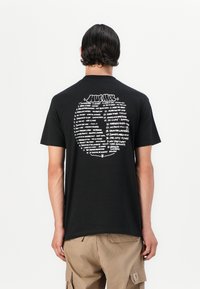 Black cotton T-shirt with short sleeves, featuring white text in varying fonts on the back listing song titles in a circle design.