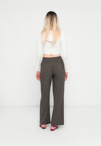 Grå vide bukser med teksturstoff, elastisk talje, sammen med en hvid cropped sweater, båret med røde sandaler.