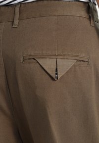 Bruna byxor med en delvis öppen bakficka som visar en liten del av ett mörkt objekt inuti.