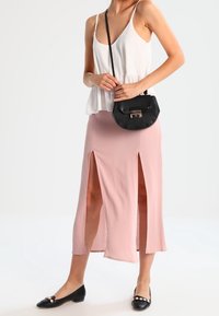 Haut sans manches blanc avec un ourlet évasé, associé à une jupe midi rose clair avec deux fentes jusqu'à la cuisse. Sac à main noir et ballerines.