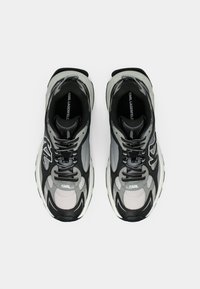 Μαύρα και γκρι αθλητικά παπούτσια με πλέγμα, χοντρή σόλα και κορδόνια. Διαθέτουν λογότυπο στη γλώσσα και χαρακτηριστικές υφασμάτινες λεπτομέρειες.