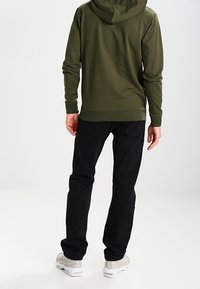 Oliivinvihreä huppari, mustat housut, harmaat lenkkitossut. Sileä kangas, rento istuvuus, yksinkertainen muotoilu, tavallinen tasku ja siistit reunat.