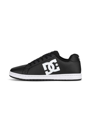 Zapatilla negra de corte bajo con suela blanca y gran logo blanco de DC en el lateral, con cordones negros y cuello acolchado.