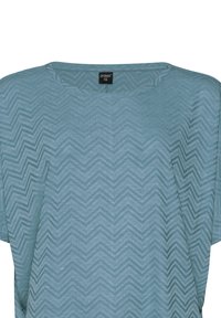 Šviesiai mėlynas tekstilinis viršus su zigzagų raštu, turi apvalų iškirpę ir trumpas rankoves, pagamintas iš minkštos, šiek tiek tekstūruotos medžiagos.