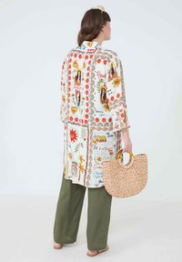 Flowy white tunic with colorful floral and graphic prints, paired with olive green wide-leg pants and a woven tote bag.