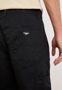 Pantalons cargo noirs en tissu durable, avec une poche en forme de cœur comportant le logo "Carhartt WIP" à l'arrière.