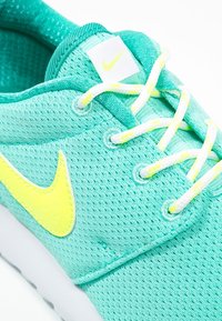 Turkos Nike-sneaker med ovandel i mesh, med en gul swoosh och klara gula snören. Vit gummisula och vadderad krage.