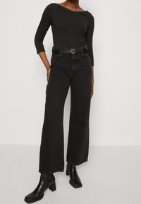 Svart långärmad bodysuit med asymmetrisk halsringning, kombinerad med högmidjade svarta vida jeans och klumpiga svarta klackstövlar.