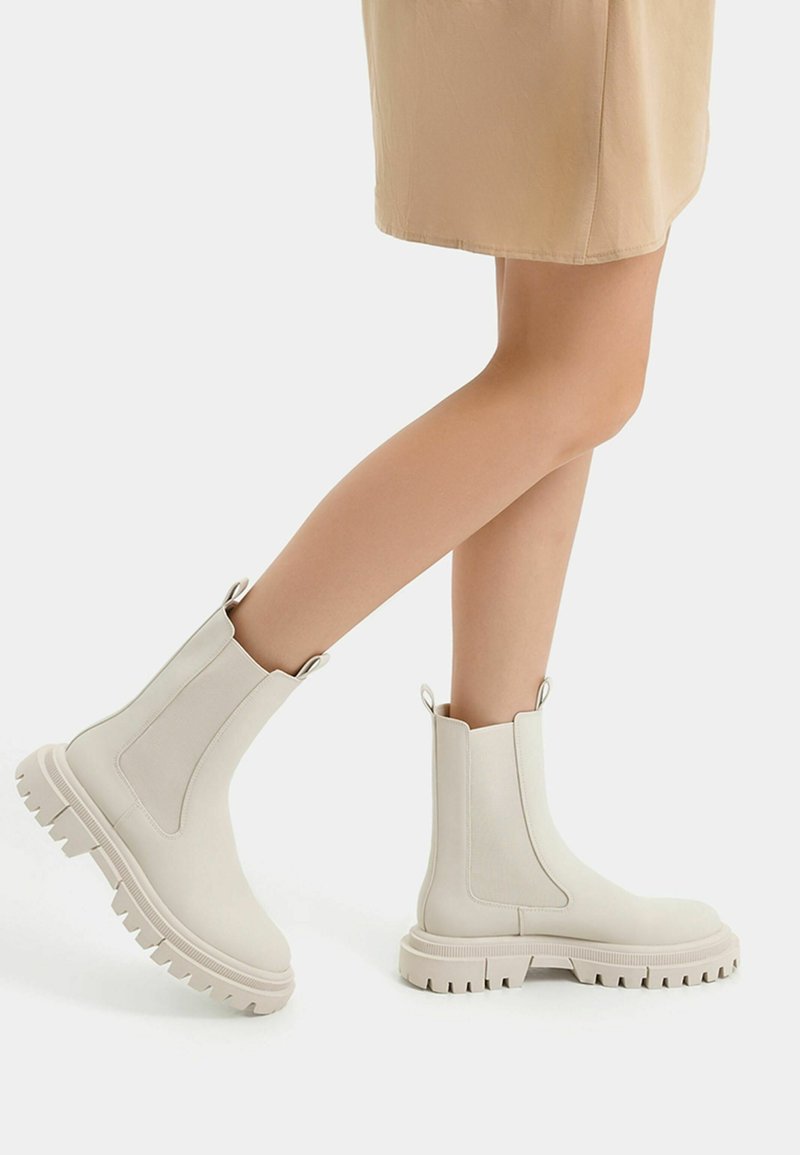 White ankle boots with chunky soles, elastic side panels, and pull tabs. Smooth texture and rounded toe design.