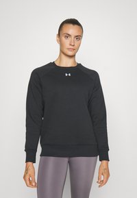 Sudadera negra con escote redondo y mangas raglán. Presenta un pequeño logo blanco en el pecho. Textura de tela suave, ajuste casual.