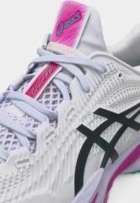 Λευκό και ρόζ αθλητικό παπούτσι ASICS με πλέγμα πλέξης, μαύρες λωρίδες λογότυπου και λεπτομέρεια με κορδόνια.