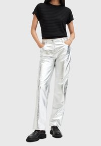 Pantalones anchos metálicos plateados con una textura suave, combinados con una camiseta corta a rayas negras y zapatos negros de suela gruesa.