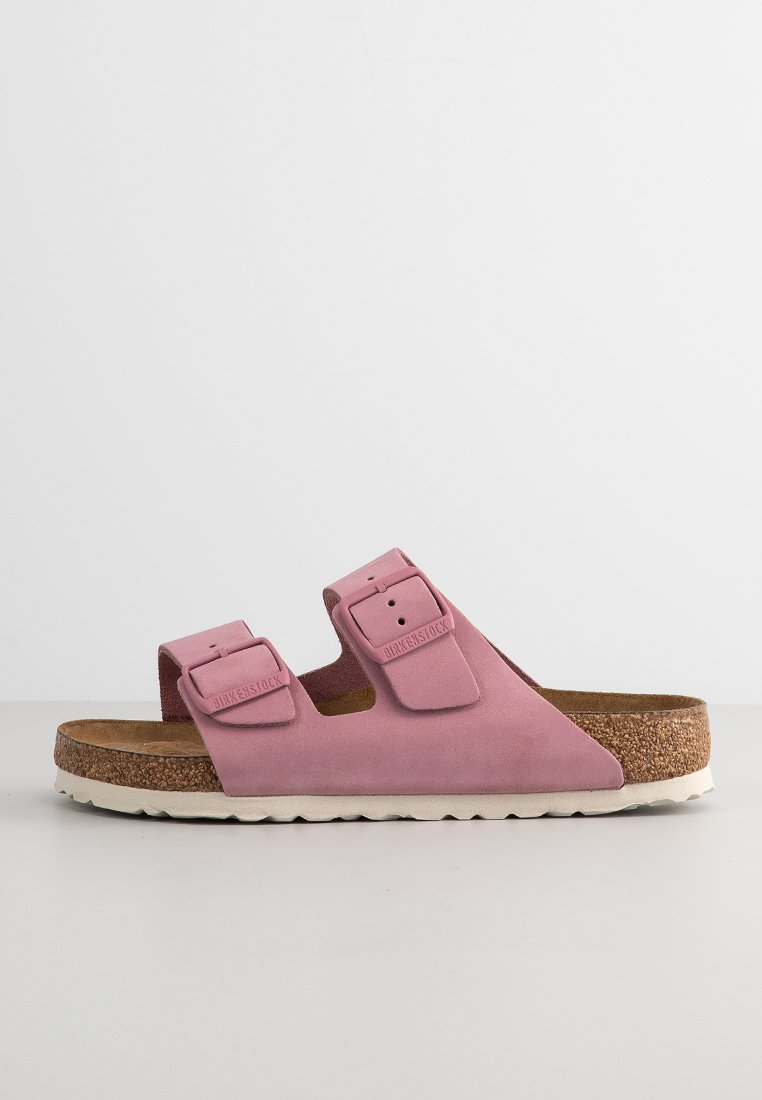 Rosa Birkenstock-Sandale mit zwei verstellbaren Riemen, Korkfußbett und weißer Gummisohle auf einer schlichten grauen Oberfläche.