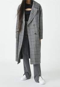 Mustavalkoinen ruutukuvioitu villasekoitetakki, jossa on kaksirivinen napitus, leveät kaulukset ja sivutaskut. Päällä musta toppi ja farkut.