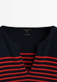 Navy blue knitted sweater with red horizontal stripes, V-neck design, and ribbed texture. Label on inner neck with brand and origin details.