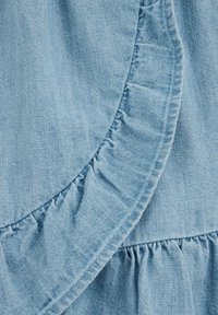 Hellblauer Denim-Stoff mit fransigen Kanten und einer glatten Textur, ergänzt durch geraffte Details entlang der Nähte für zusätzliche Dimension.