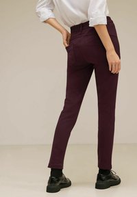 Burgundy housut, joissa on vartalonmyötäinen muotoilu ja joustava vyötärö. Niissä on kaksi takataskua ja ne on yhdistetty mustiin kenkiin.