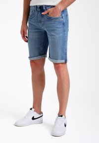 Lichtblauwe denimshorts met opgerolde mouwen, vijf zakken, een slim fit en een licht vervaagde textuur. Gemaakt met witte sneakers.
