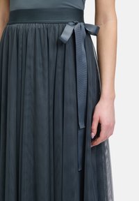 Jupe en tulle gris foncé avec un design doux et fluide, dotée d'une large taille et d'un détail de lien en ruban. Le tissu semble léger et texturé.