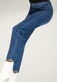 Jeans de denim azul con una silueta ajustada, cintura de altura media y un ligero desvaído. Combinados con botas tobilleras blancas, con un detalle de cremallera.