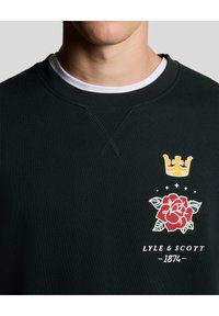 Dunkelgrüner Sweatshirt mit Rundhalsausschnitt, das eine Krone und eine Rose in Rot und Gelb zeigt, sowie den Text "LYLE & SCOTT 1874" darunter.
