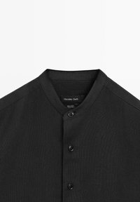 Czarna lniana koszula z kołnierzykiem typu stójka i trzema czarnymi guzikami z przodu, z metką Massimo Dutti wewnątrz kołnierza.