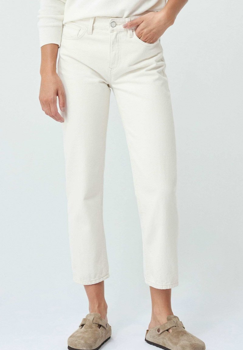 Jeans de denim blanco con un corte recto, cintura alta, diseño de cinco bolsillos y un ligero desgastado. Combinados con zapatos en color beige tipo slip-on.