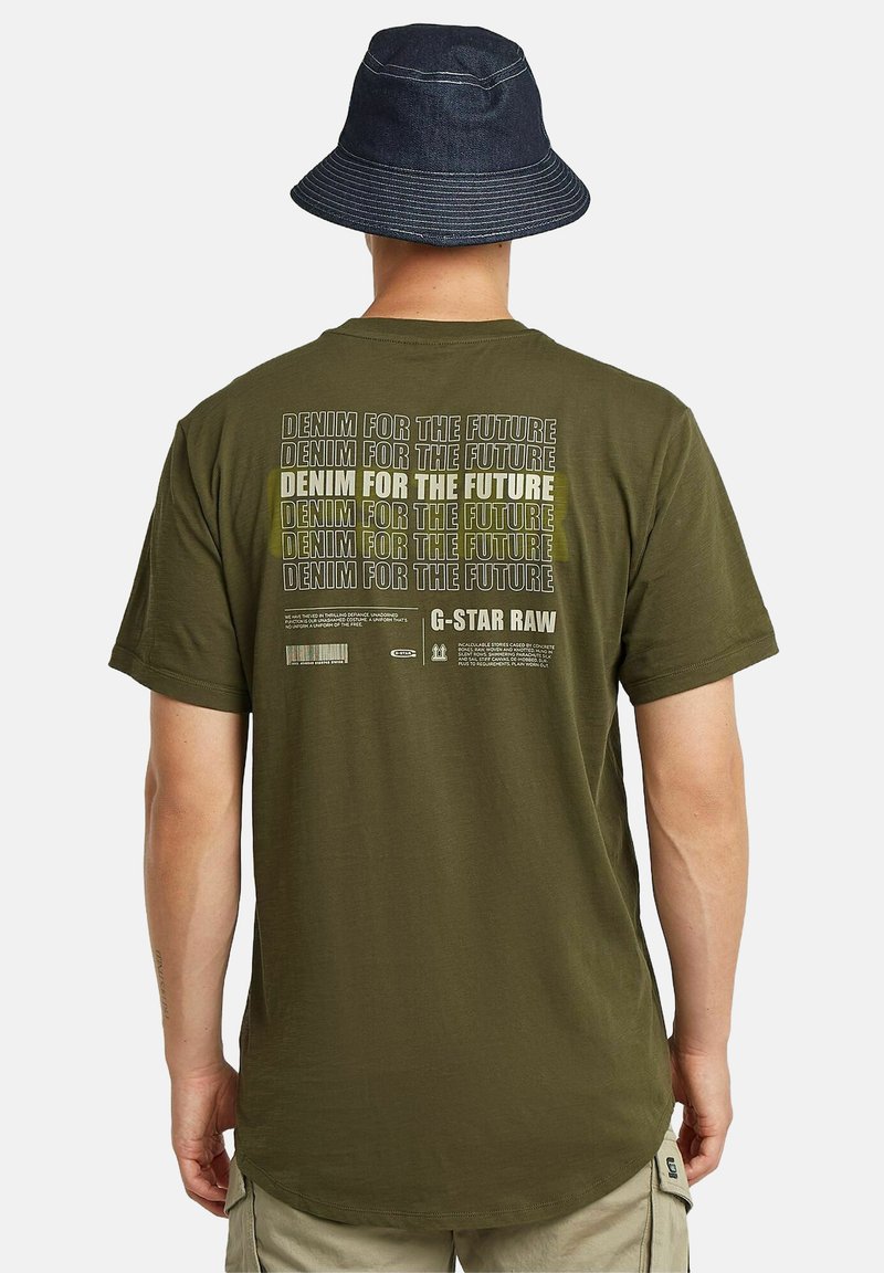 Camiseta verde oliva con un gran estampado gráfico en la parte posterior con el texto repetido "DENIM PARA EL FUTURO". Tejido suave y corte relajado.