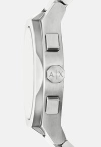 Orologio in acciaio inossidabile con corona esagonale, due pulsanti e una superficie liscia e riflettente. Presenta un design minimalista e una forma angolare.