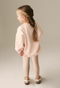 Ljust rosa oversized sweatshirt med ribbade ärmar, kombinerad med tan- och krämrandiga leggings. Skorna har lätta remmar och en platt sula.