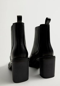Stivaletti neri in pelle con finitura testurizzata, caratterizzati da righe verticali, un tacco squadrato spesso e linguette per una facile calzata.
