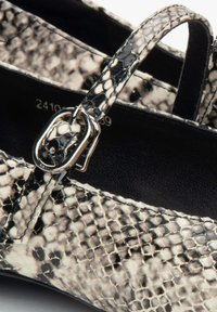 Zwart-wit slangenhuidpatroon neplederen schoen met een slanke band en metalen gesp detail, die een gladde textuur toont.