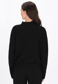 Czarny, oversize sweter z wysokim kołnierzem, wykonany z puszystego materiału. Posiada długie rękawy i ściągacz na dole; miękka tekstura i luźny krój.