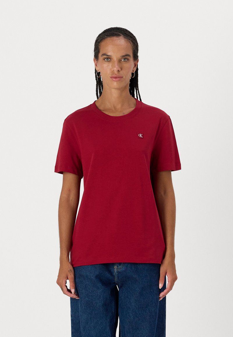 Μαρόν βαμβακερό t-shirt με κοντά μανίκια, στρογγυλή λαιμόκοψη και μικρή λογότυπη ετικέτα στο στήθος. Συνδυασμένο με μπλε τζιν παντελόνι.