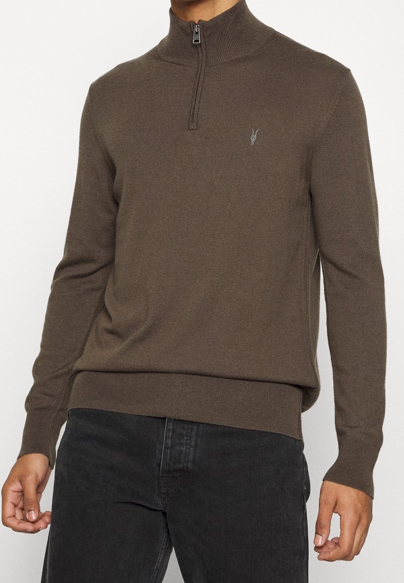 Hnědý svetr na zip s žebrovanými manžetami a lemem. Vyrobený z měkkého materiálu, s malým logem na hrudi a vysokým límcem.