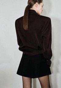 Blazer marrón ajustado con un corte relajado, combinado con pantalones cortos negros. Tejido suave, diseño minimalista y silueta elegante.