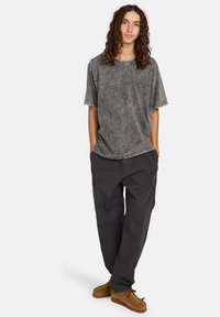 Camiseta gris de gran tamaño con textura desvaída, mangas cortas y costuras en contraste, combinada con pantalones cargo oscuros y zapatos de ante marrón.