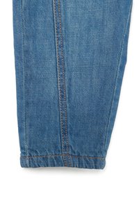 Gamba di pantaloni in denim blu con design dritto, cuciture visibili in marrone a contrasto e polsino arricciato all'orlo.